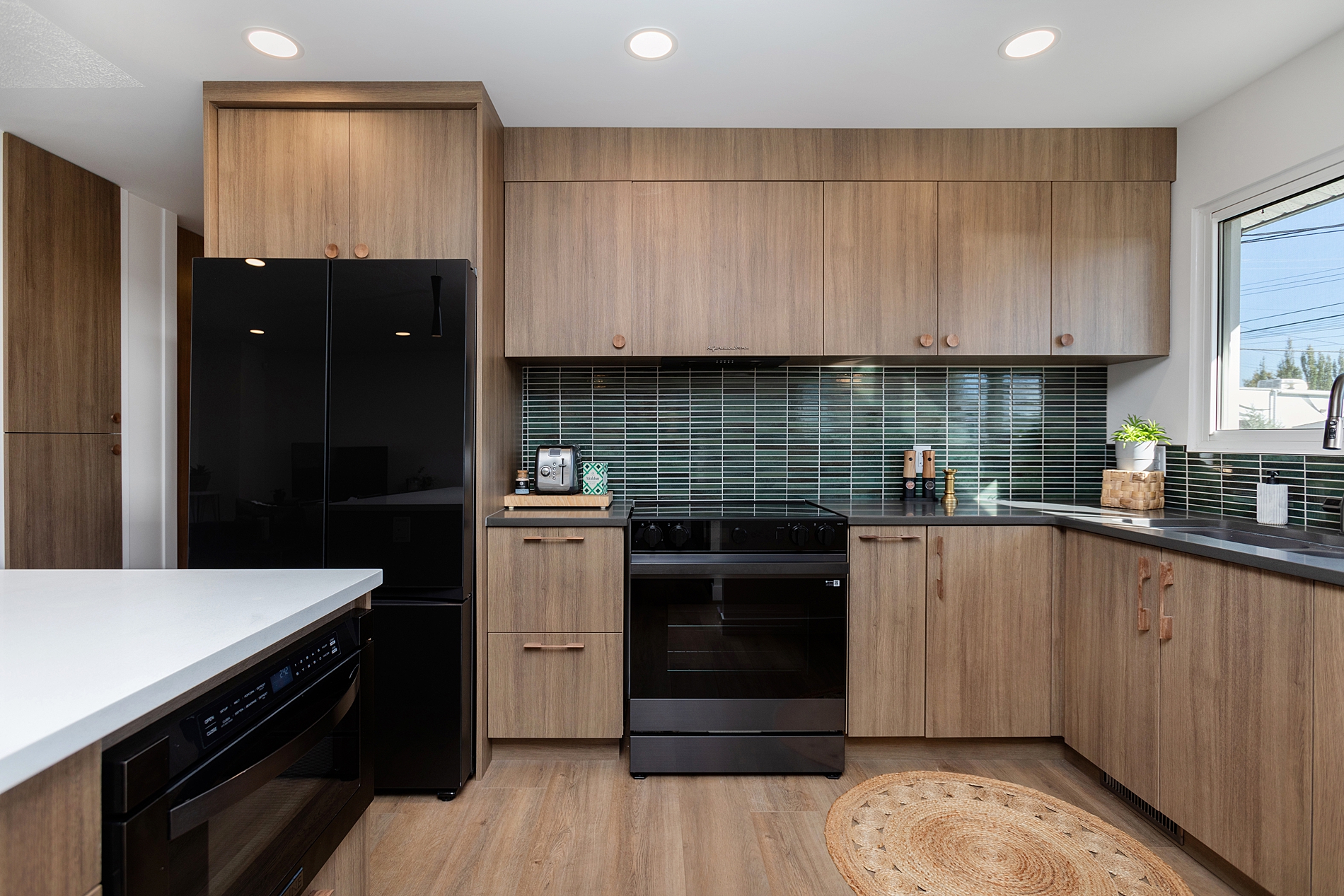 A mid-century modern kitchen renovation in Edmonton, with walnut wood cabinets, Quartz countertops, wood floors and a linear tile backsplash. This kitchen renovation was part of a whole main floor renovation and update that was completed by Awlridge Renovations.