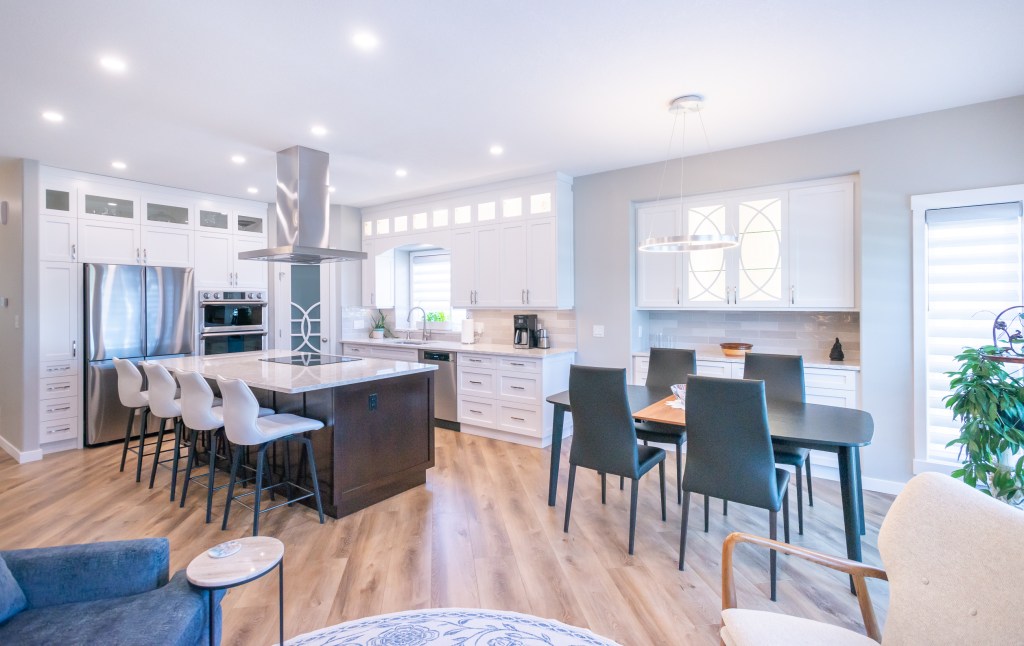 View of a Kitchen Renovation and dining area with an open concept in Spruce Grove Alberta, with modern cabinetry, large island, quartz countertops and new hardwood flooring. This kitchen renovation was part of a whole main floor renovation and update that was completed by Awlridge Renovations.