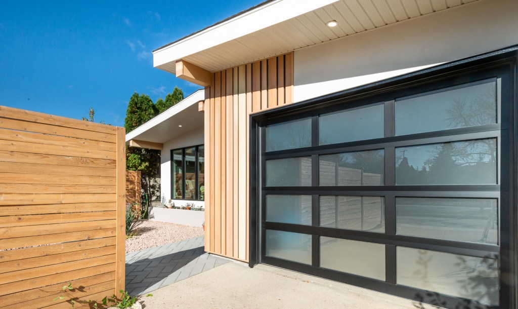 Modern Exterior Renovation on a home in Edmonton, with wood grain, metal siding accents (installed vertically), white acrylic stucco finish and new windows and doors with a black colored frames.  This exterior renovation was completed by Awlridge Renovations.